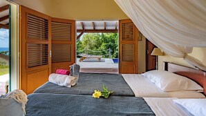 Ein Zimmer mit zwei Betten, einer Hängematte und Blick auf grüne Vegetation.