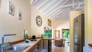Eine moderne Küche mit Spüle aus Edelstahl, eingebautem Herd und Kühlschrank. An der Wand hängt eine Uhr und ein Fenster bietet Blick auf einen Garten.
