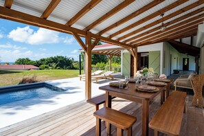 Una terraza de madera con piscina, mobiliario exterior y un patio cubierto.