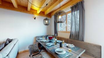 Un comedor con mesa de madera dispuesta para cuatro personas, un sofá y una ventana con cortinas.