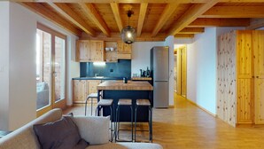 Una cuina moderna amb bigues de fusta, una illa central, tamborets i un frigorífic.