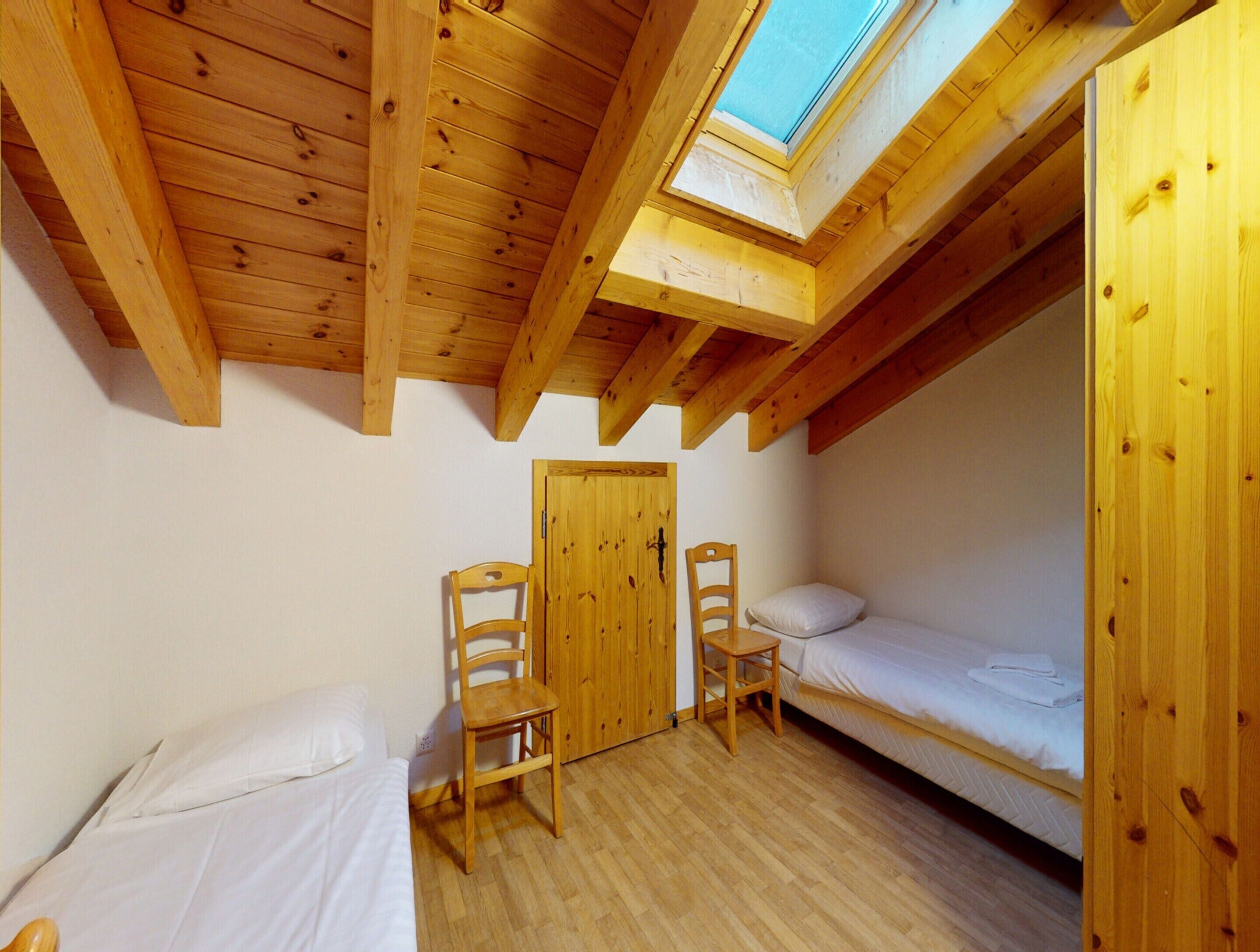 A small, wooden room with two beds, a skylight, and a door.