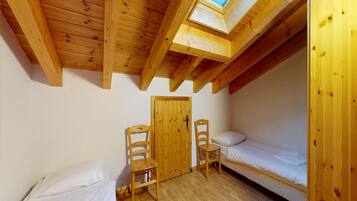 A small, wooden room with two beds, a skylight, and a door.