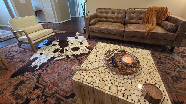 Una sala de estar con un sofá de cuero, una mesa de centro de madera con una vela y un tapiz de cuero de vaca.