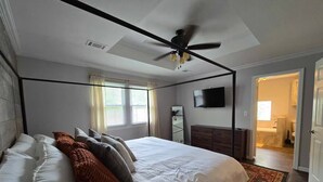 Un dormitorio con cama con dosel, ventilador de techo, televisor y vestidor.