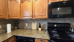 Una cocina con armarios de madera, encimera de granito, estufa negra y microondas.