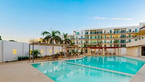 A swimming pool with lounge chairs and umbrellas, surrounded by a white wall and a multi-story building with balconies. - Apartment C25, if you are looking for tranquility, this is the right place for you!  (San José del Cabo)