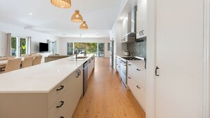 Une cuisine moderne avec des meubles blancs, un îlot central, des luminaires suspendus et une vue sur la verdure à l’extérieur.