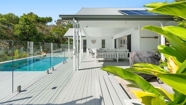 Une maison moderne dotée d’une piscine, d’un espace salon extérieur couvert et de panneaux solaires sur le toit.