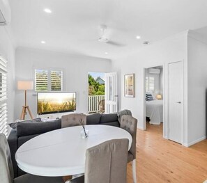 A modern living room with a round dining table, grey sofas, and a flat-screen TV.