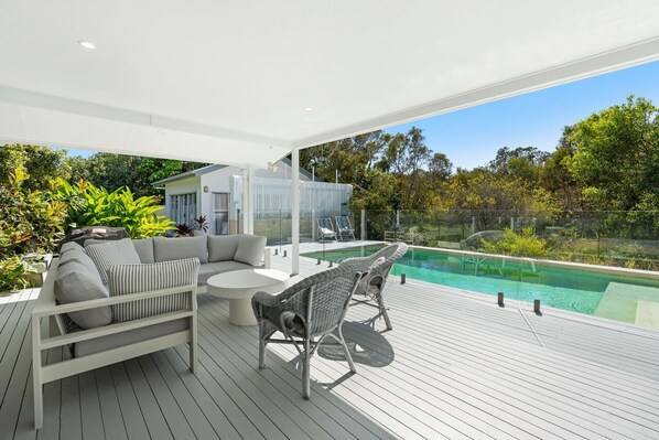 A modern outdoor deck with a pool, seating area, and glass enclosure.
