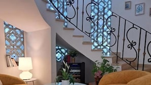 Uma sala de estar moderna com uma escada em espiral, uma mesa redonda com planta em vaso e dois pufes amarelos.