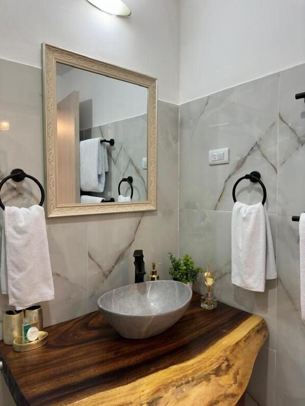 Un baño con salpicadero de mármol, tocador de madera, un espejo grande y dos toalleros con toallas blancas.