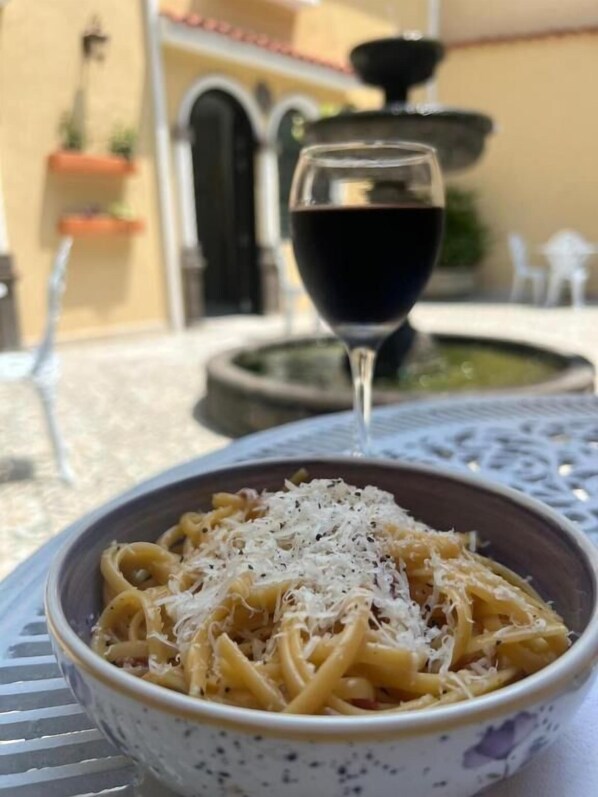 A bowl of pasta with grated cheese, a glass of red wine, and a fountain in the background. - Casa Sileo (Cali)