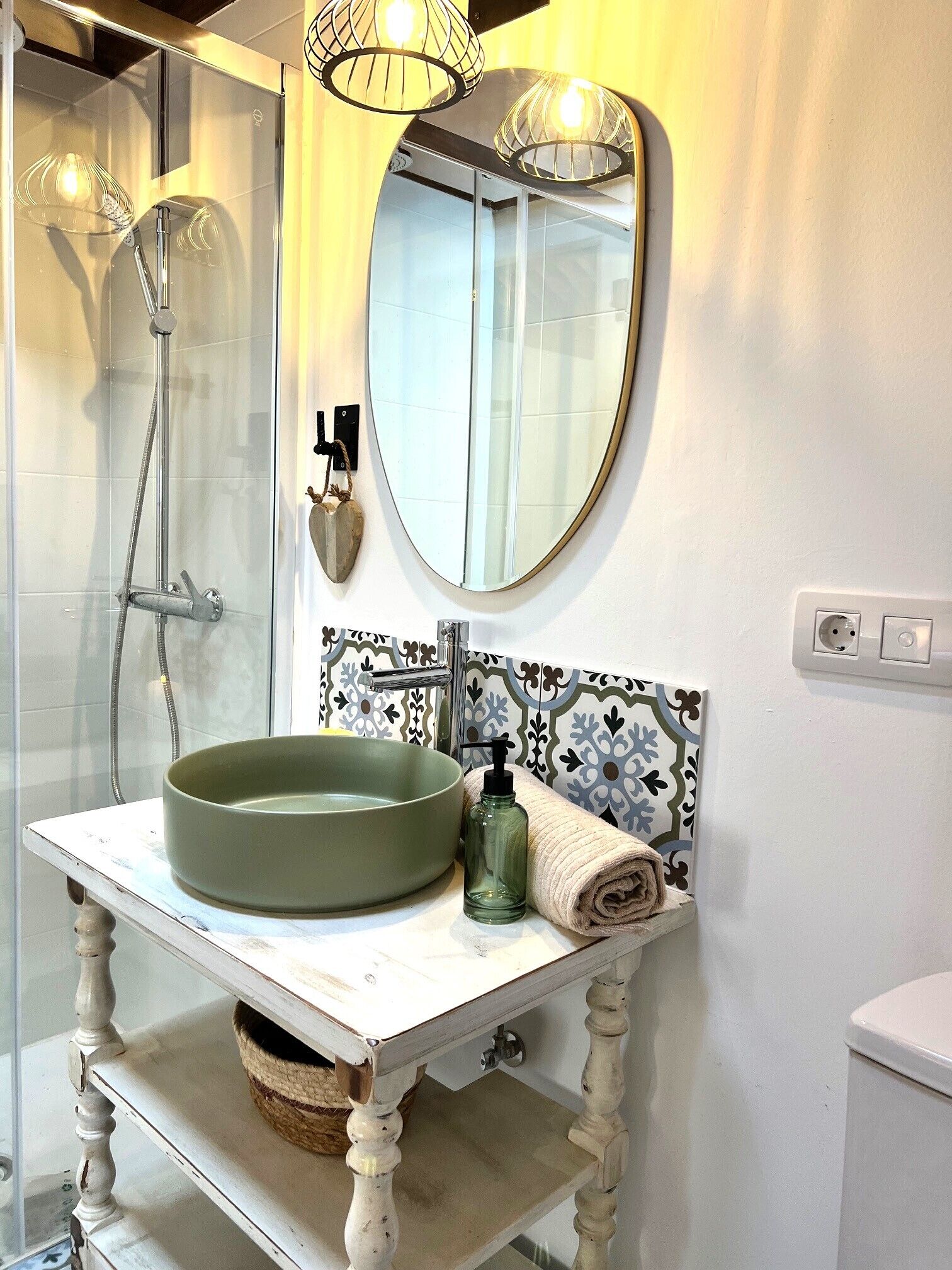 Une salle de bain dotée d’une douche à parois de verre, d’un lavabo rond avec un receveur vert, d’un miroir au-dessus du lavabo et d’un pare-feu en carreaux décoratifs.
