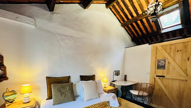Un dormitorio acogedor con cama, almohadas, una mesita de noche con lámpara, una pequeña mesa con silla y una puerta de madera.