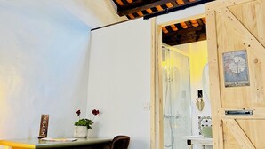 Una habitación con techo inclinado, una puerta de madera, un escritorio pequeño con una silla, una planta en maceta y un letrero en la pared.