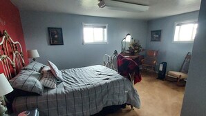Une chambre à coucher avec un lit, un bureau, une chaise, deux fenêtres et un mur rouge.