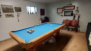 Une table de billard avec des billes, un canapé et des éléments de décoration murale dans une pièce dont le sol est recouvert de moquette.