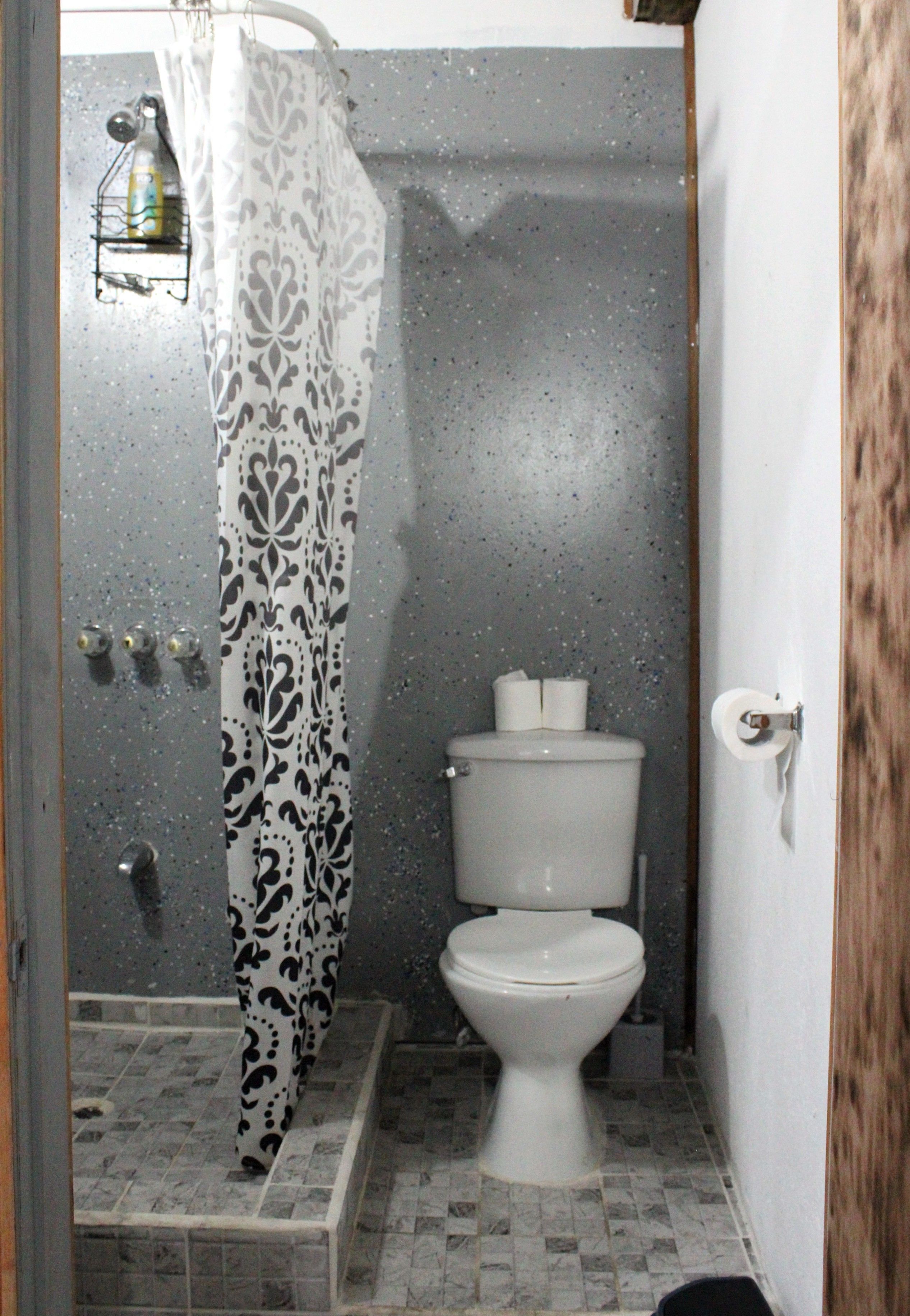 Un bagno con tenda doccia, toilette e pavimento piastrellato.