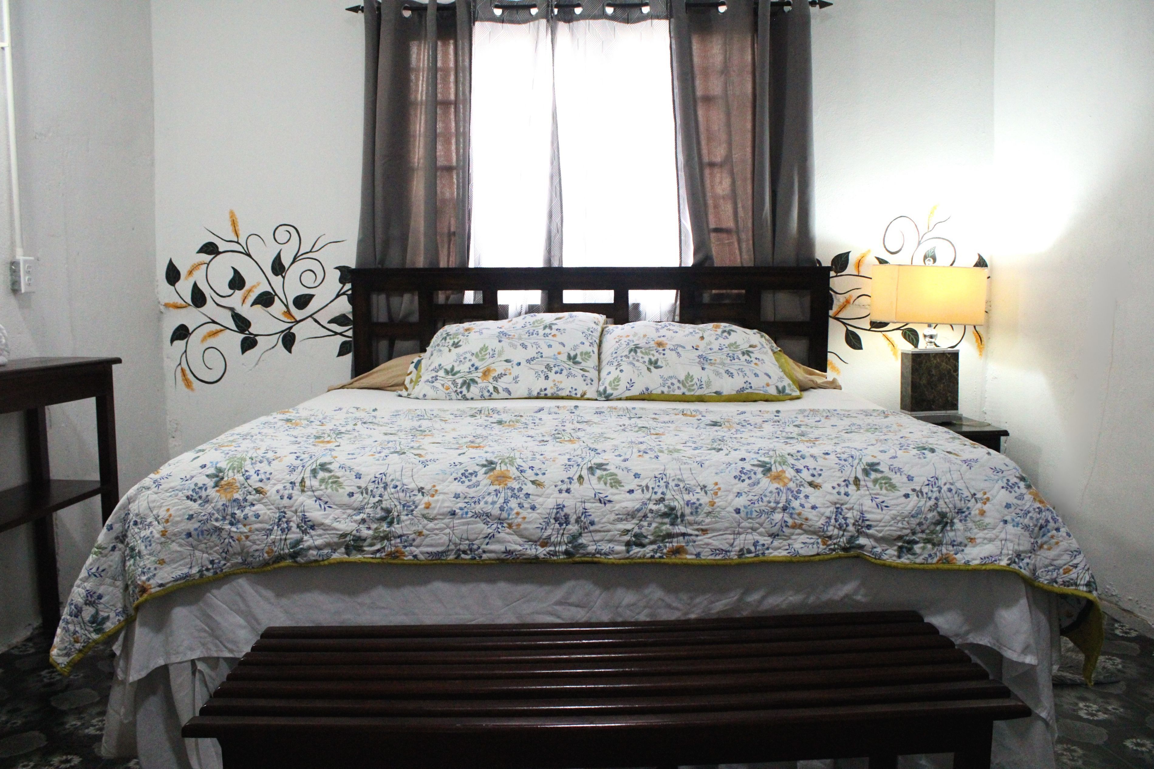 Un lit avec une couvre-lit à motifs floraux, une tête de lit en bois et une lampe de chevet.