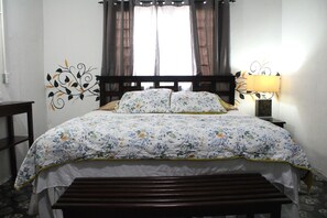 A bed with a floral bedspread, a wooden headboard, and a bedside lamp. - D's Inn (San Ignacio)