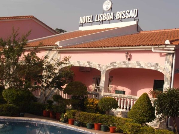 Een roze gebouw met een bord waarop 'HOTEL LISBOA BISSAU' staat.