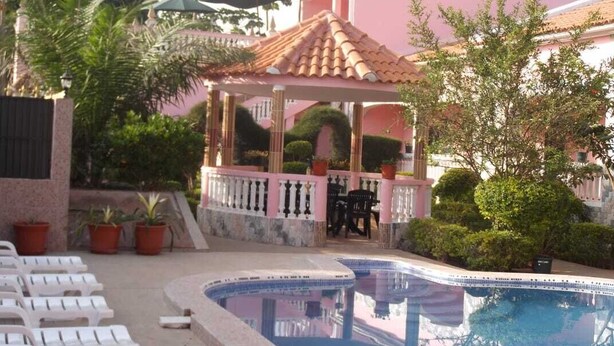 Une piscine avec des chaises longues, un kiosque et des plantes en pot.