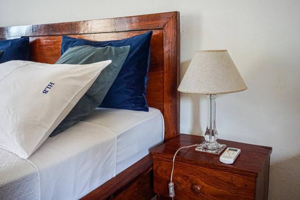 A neatly made bed with a white pillow labeled "BTH" and a wooden nightstand with a lamp and a phone.