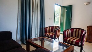 Un salon avec une table basse en verre, deux fauteuils à rayures, un canapé et une porte verte donnant sur l’extérieur.