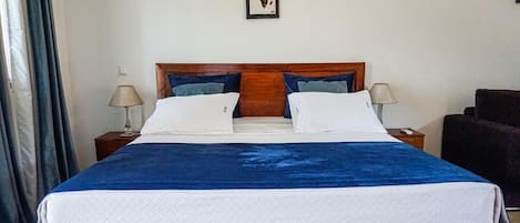 Uma cama bem arrumada com colcha azul e branca, duas luminárias de cabeceira e um quadro na parede.