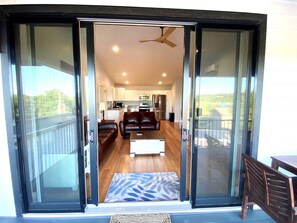 A modern living room with a sofa, a coffee table, and a view of the kitchen through glass doors.