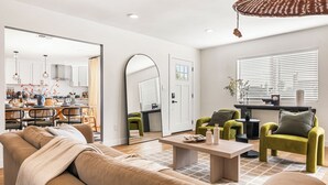 En moderne stue med sofa, lænestole, et sofabord og et spiseområde med et køkken i baggrunden.