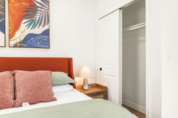 A neatly made bed with a red headboard, a bedside lamp, and a small wooden nightstand.