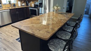 A kitchen with granite countertops, dark cabinets, stainless steel appliances, and a central island with bar stools.