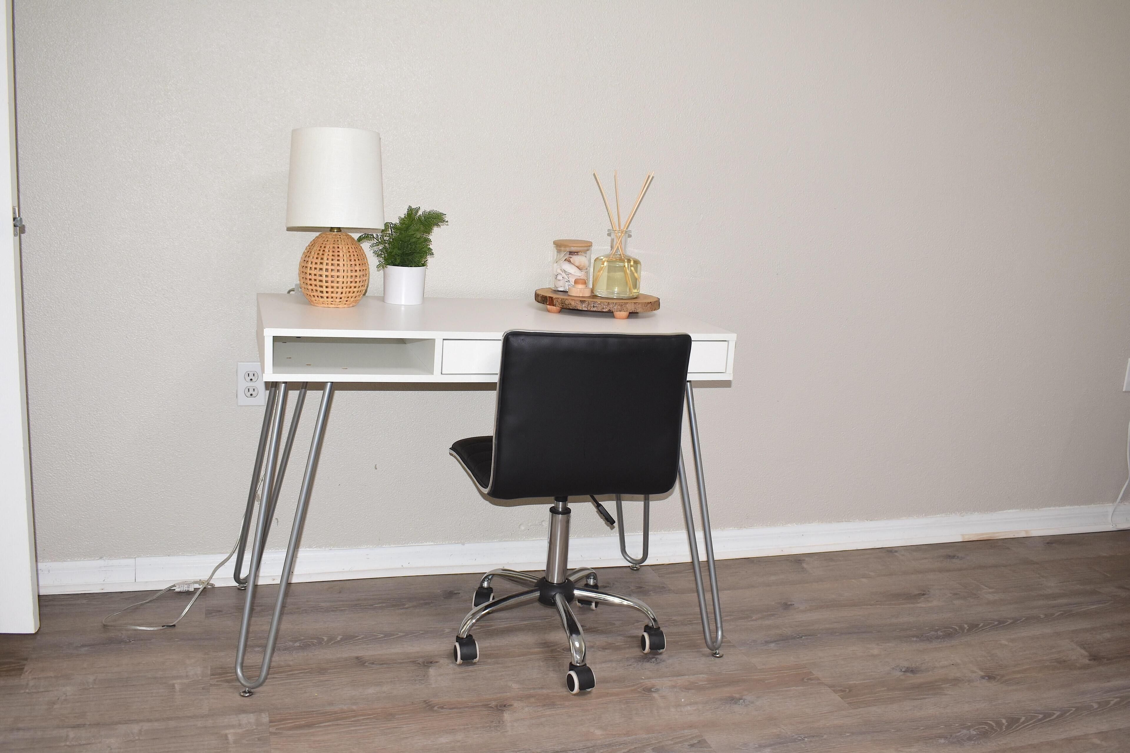 A white desk with a black office chair, a lamp, a small potted plant, and a decorative tray with a glass jar and reed diffuser.