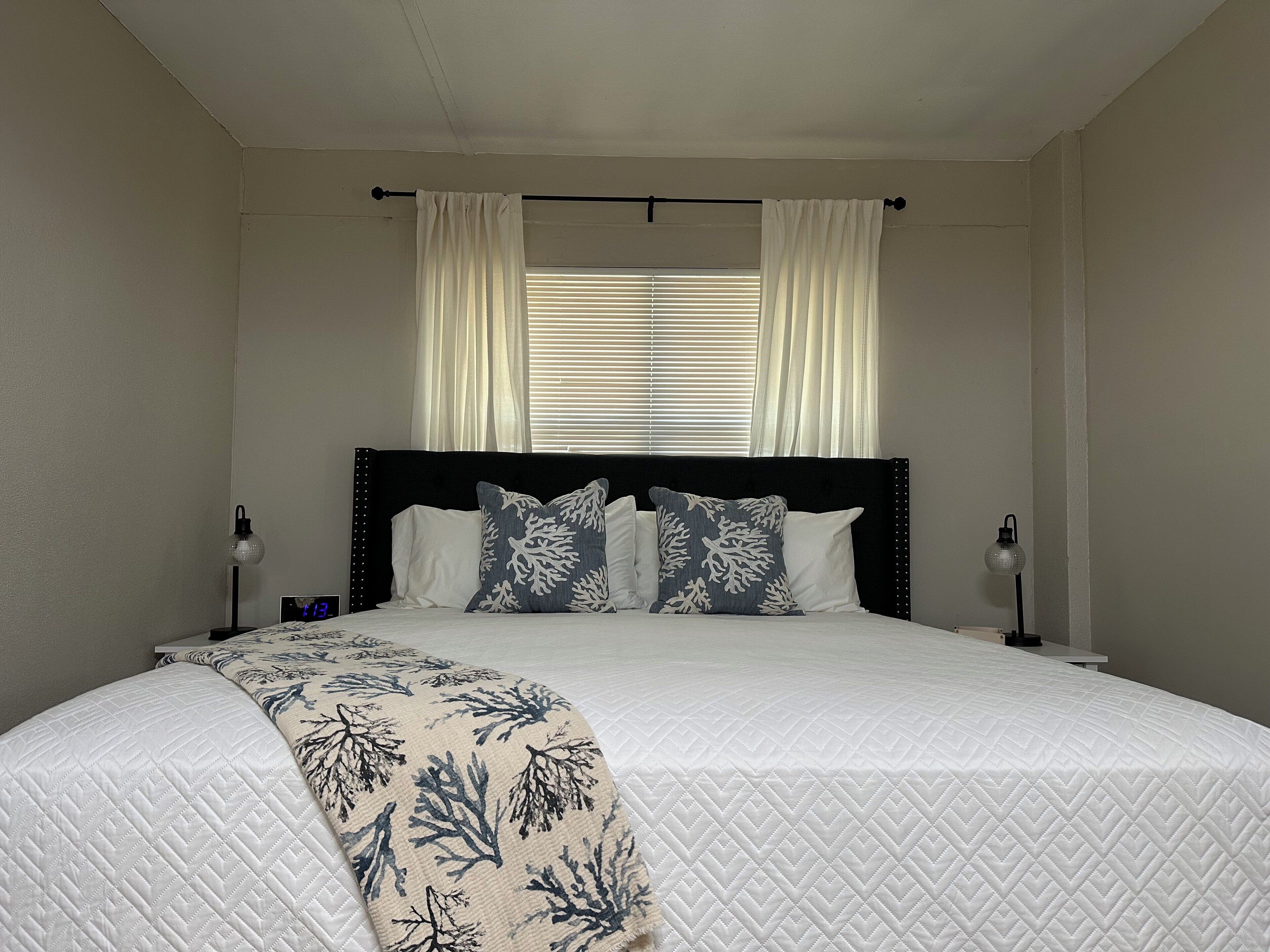 A neatly made bed with a quilted white duvet, two pillows with a blue and white coral pattern, and a matching throw blanket.