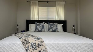 A neatly made bed with a quilted white duvet, two pillows with a blue and white coral pattern, and a matching throw blanket.