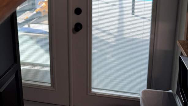 A door with a glass panel, a hand pointing at it, and a view of a swimming pool outside.