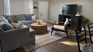 A living room with a sofa, armchair, ottoman, TV stand, and a ceiling fan.