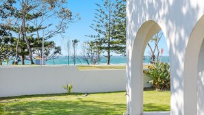 A coastal view with a white building, a pathway, and a small plant. - Beach Front Beach Break - Entire Home (Byron Bay)