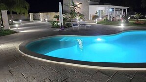 Ein Schwimmbecken mit einer terrassebelag aus Stein, umgeben von einem Gebäude mit Außenbeleuchtung.