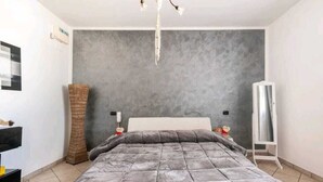 Ein Schlafzimmer mit einem großen Bett, einer grauen Wand mit Struktur, einem hohen gewobenen Korb, einem weißen Nachttisch und einem weißen Kleiderschrank.