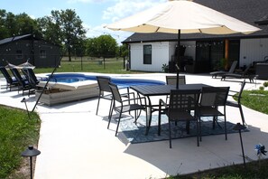 An outdoor patio with a pool, lounge chairs, and a table with chairs. - Modern Family Getaway! Heated Pool, Hot tub Theatre Room, Game room! (Joplin)