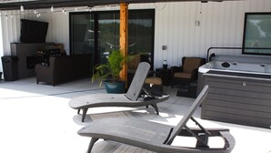 Une terrasse extérieure avec des fauteuils de jardin en osier, un jacuzzi et une plante en pot.