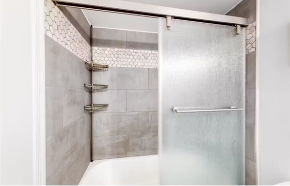 A modern bathroom with a glass shower enclosure, grey tiles, and a metal towel rack. - On the beach! Peaceful, private, gated patio, oceanfront! (Ocean City)