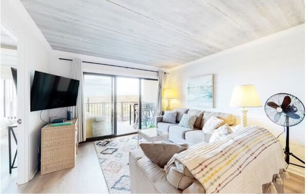 A modern hotel room with a large bed, a flat-screen TV, a balcony with a view, and a fan.