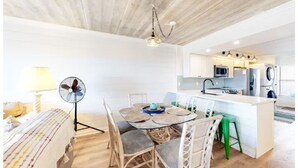 Uma cozinha moderna com armários brancos, uma ilha central e uma área de refeições com uma mesa redonda e cadeiras.