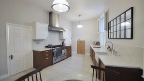 A modern kitchen with white cabinets, a stainless steel range hood, and a central island with bar stools. - Ramsgate - Coastal Cottage Escape - Pet Friendly with Parking (Ramsgate)