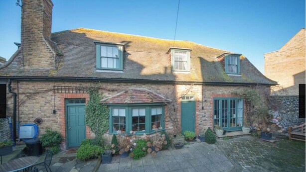 A traditional brick house with a tiled roof, two windows with green frames, and a small garden area with potted plants and a stone patio. - Ramsgate - Coastal Cottage Escape - Pet Friendly with Parking (Ramsgate)